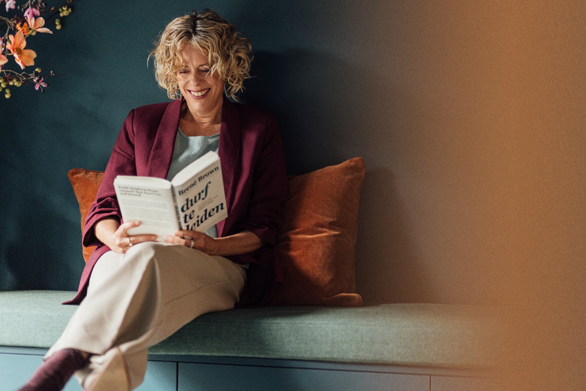 Ann Verlinden leest een boek op een warme zitbank in een ruimte met petrolkleurige wand