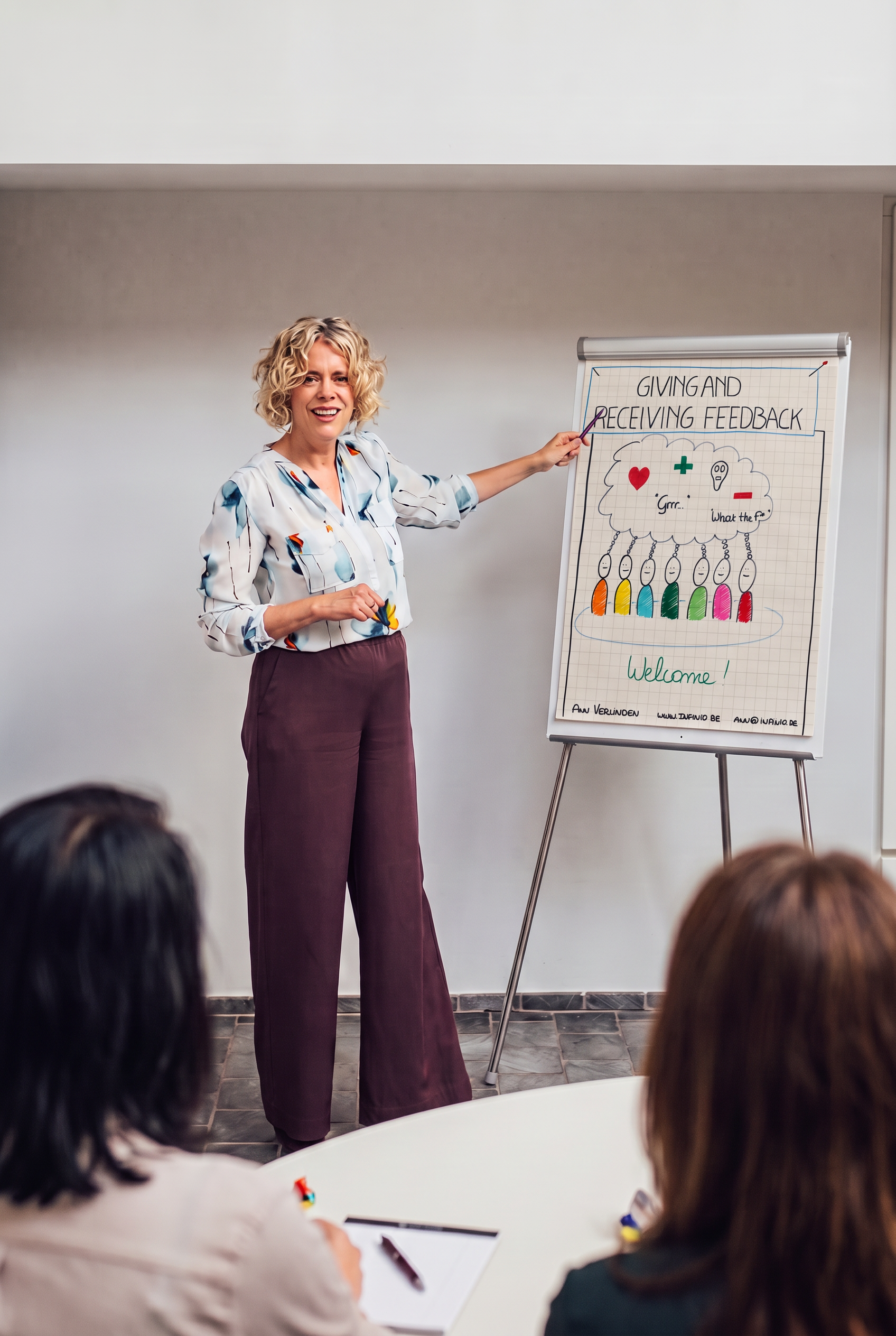 Ann Verlinden in een trainingssituatie, wijzend naar een flip-over met handgetekende inzichten over giving and receiving feedback
